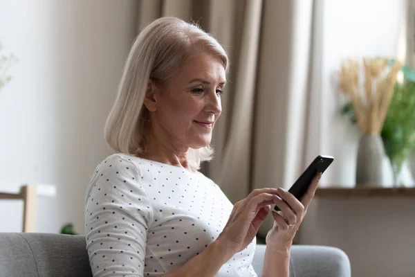 Счастливая женщина средних лет использует мобильные приложения смс дома — стоковое фото