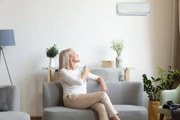 Mujer de mediana edad encendiendo el aire acondicionado en el salón — Foto de Stock