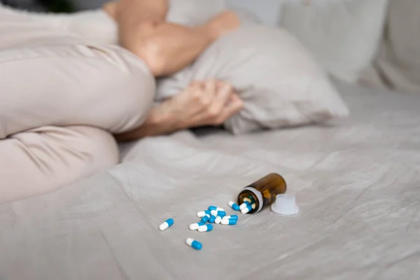 Donna depressa sdraiata che copre con cuscino vicino pillole sul letto — Foto Stock