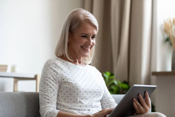 Sorridente donna anziana in possesso utilizzando tablet digitale rilassante a casa — Foto Stock