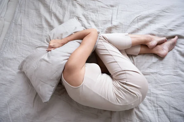 Wanita dewasa ketakutan berbaring di tempat tidur posisi janin meliputi bantal — Stok Foto