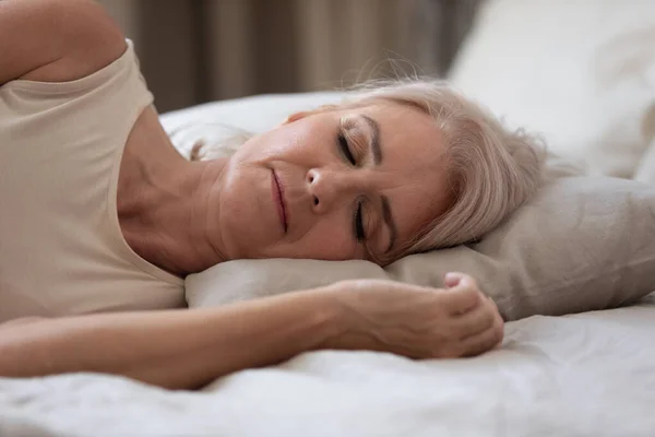 Calm serene older woman sleeping alone in bed, closeup view — Stock Photo, Image