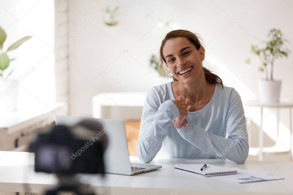 Smiling woman sitting at table in front of digital camera.