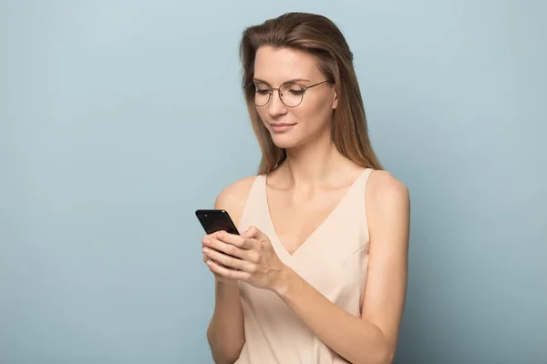 Mujer milenaria en gafas ocupadas usando un teléfono inteligente moderno — Foto de Stock