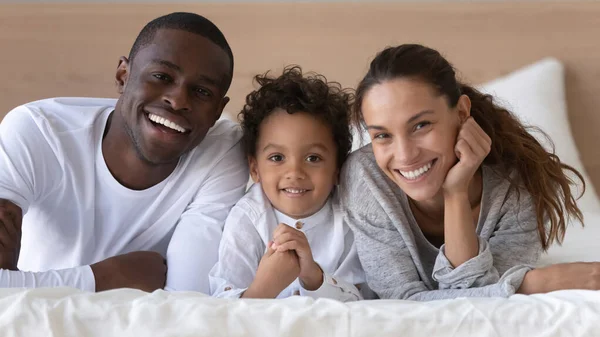 Портрет счастливой многорасовой семьи из трех человек, позирующих в спальне — стоковое фото