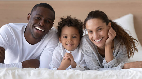 Portrait of happy multiracial family of three posing in bedroom