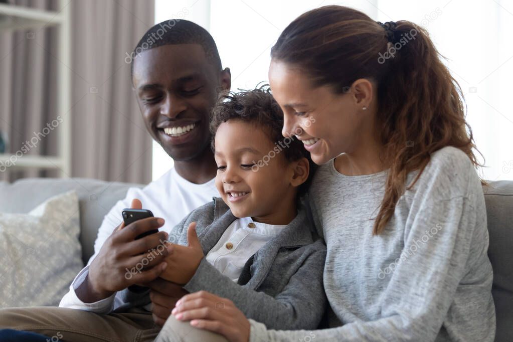 Happy multiracial parents with son using cellphone at home