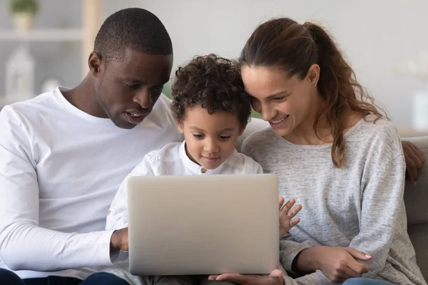 Sorrindo família internacional com criança usando laptop em casa — Fotografia de Stock