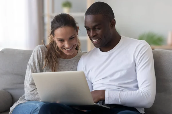 Feliz pareja internacional relajarse en casa con el ordenador portátil —  Fotos de Stock