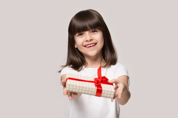 Lächelndes kleines Mädchen präsentiert verpackte Geschenkschachtel und blickt in die Kamera — Stockfoto