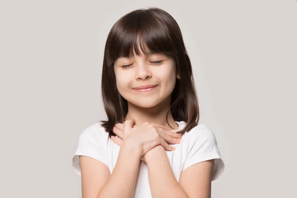 Милая маленькая девочка с руками на груди молится — стоковое фото