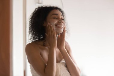 Mutlu Afrikalı Amerikalı kadın banyoda cilt bakım maskesi takıyor..