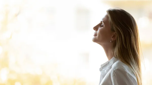 Calm happy business woman breathing fresh air stand at window