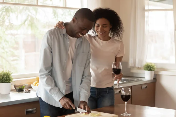 Mutlu bir eş, bir bardak şarapla yemek pişiren kocasının yanında duruyor.. — Stok fotoğraf