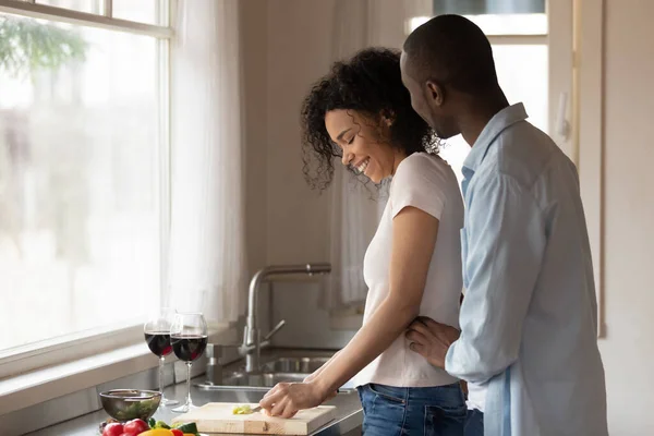 Happy man cuddling cheerful black woman preparing food. — Stok fotoğraf