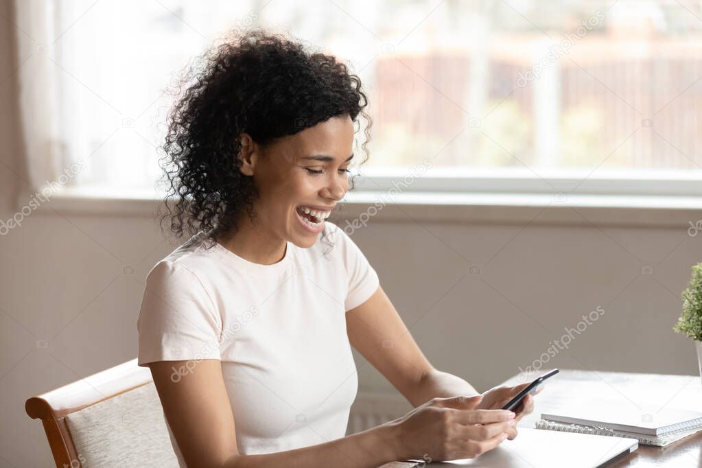 Overjoyed happy black young woman watching funny video on smartphone.