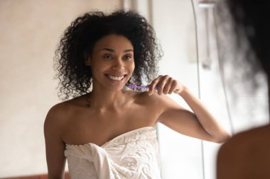 Havluya sarılı gülümseyen Afro-Amerikan milenyumu kadın diş temizliği.