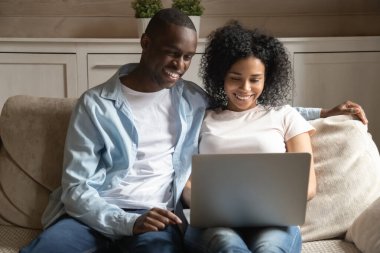 Gülümseyen Afro-Amerikan evli eşi evde dizüstü bilgisayarla oturuyor..