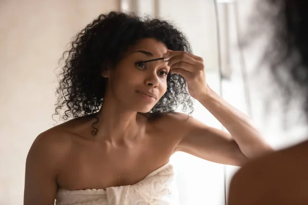 African american pleasant woman in towel applying mascara on lashes. — Stok fotoğraf