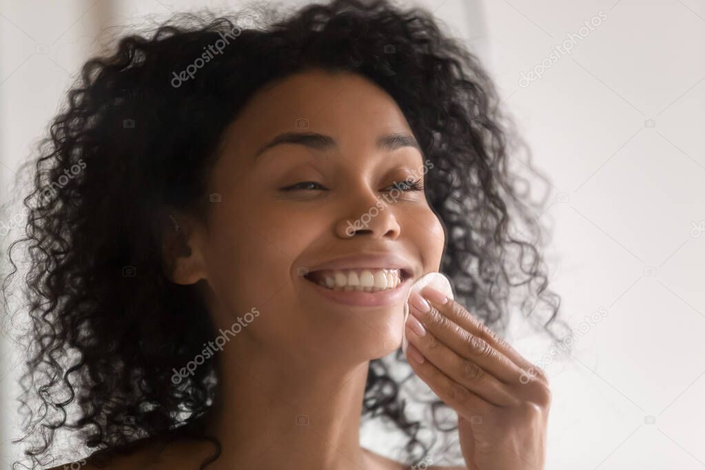 Happy african american young woman using disposable cotton pads.