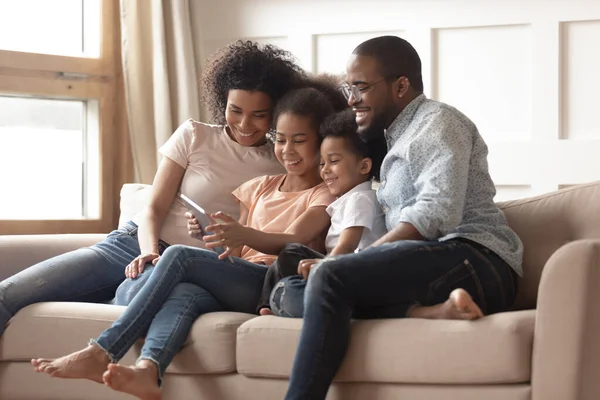 Heureuse famille noire avec enfants se détendre sur le canapé avec tablette — Photo