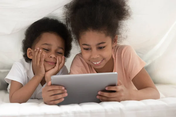 Souriant noir frères et sœurs regarder la vidéo sur tablette au lit — Photo