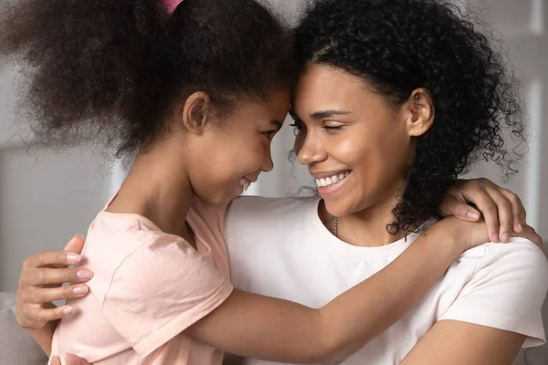 Smiling black mother and daughter look in eyes hugging — Stock Photo, Image