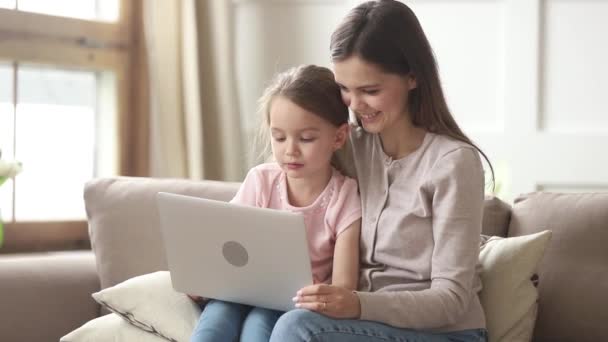 Mère assise sur le canapé avec sa fille utilisant un ordinateur portable à des fins éducatives — Video