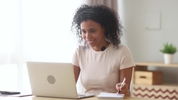 Smíšené rasy žena nosí sluchátka dělá poznámky učí on-line — Stock video