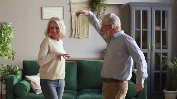 Elderly spouses listening energetic music dancing in living room — Stock Video