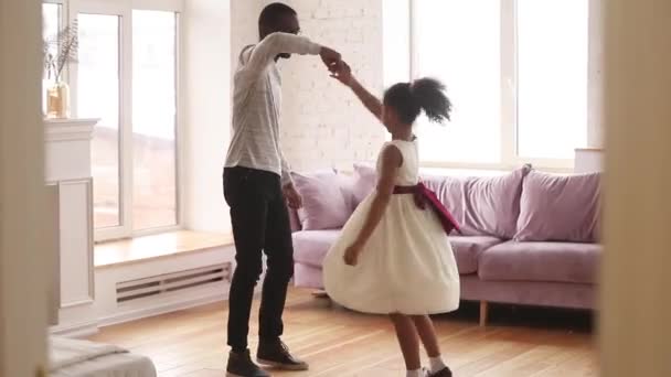 African father holding hand of daughter swirls her dancing indoors — ストック動画