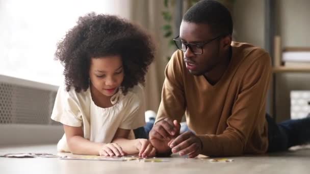 Black father and daughter collect jigsaw puzzle lying on floor — Stock Video