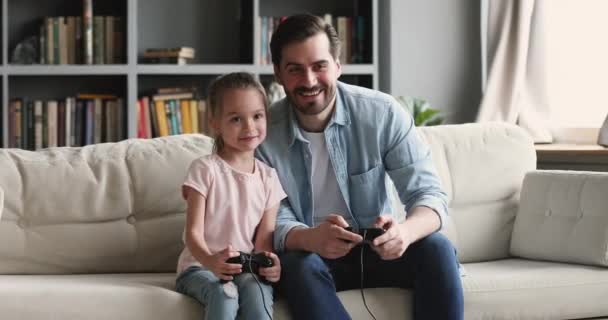 Szczęśliwy młody ojciec uczy dziewczynkę grać w gry wideo. — Wideo stockowe