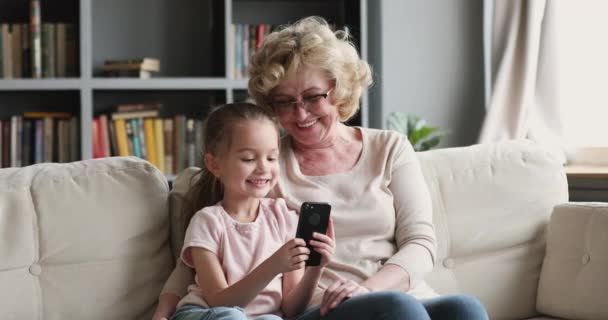 Mała wnuczka gra w gry mobilne z babcią w domu. — Wideo stockowe