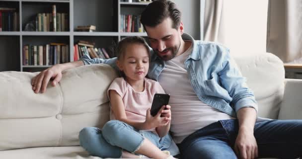 Счастливая девушка показывает смешное мобильное приложение улыбающемуся молодому отцу , — стоковое видео