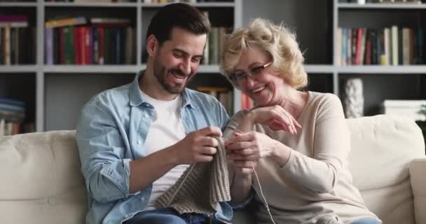 Feliz de mediana edad madre enseñanza adulto hijo tejer ropa de abrigo . — Vídeos de Stock