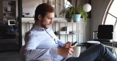 Genç işadamı akıllı telefon kullanıyor ve ofiste çay içiyor.