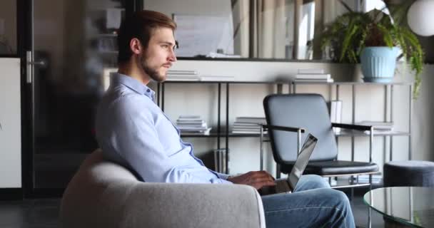 Pensativo empresario serio usando portátil sentado en la silla en la oficina — Vídeos de Stock