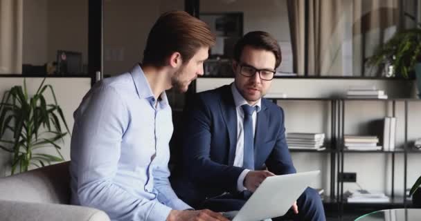 Dos hombres de negocios felices usando el ordenador portátil se dan la mano en la oficina — Vídeos de Stock