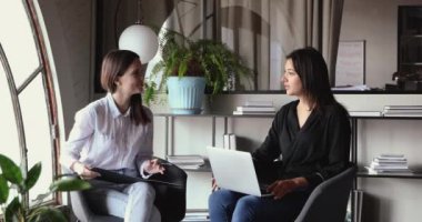 Modern ofiste sandalyede oturan iki farklı iş kadını konuşuyor.