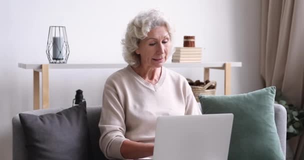 Happy focalisé senior 60 ans mamie assis sur le canapé avec ordinateur portable . — Video