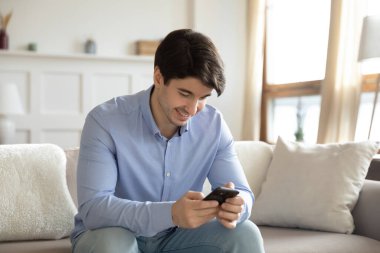 Gülümseyen genç adam evde modern akıllı telefon kullanıyor.