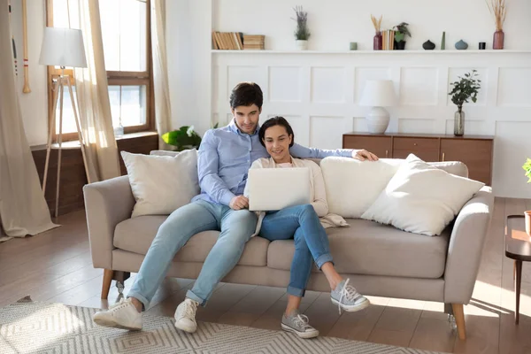 Happy Caucasian couple relax on couch using laptop