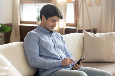 Genç adam akıllı telefon kullanarak kanepede rahatla.