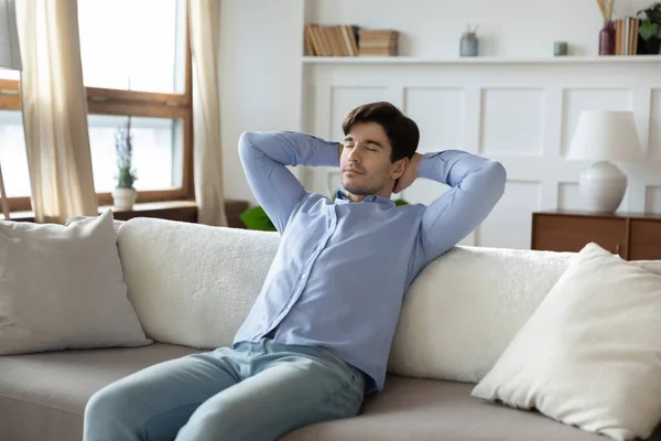 Calm caucasian man relax on sofa at home daydreaming