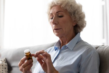 Cam şişeyi tutan yaşlı kadın hap talimatı okuyor.