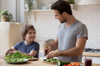 Gülümseyen küçük baba ve küçük oğlu evde birlikte yemek pişiriyor.