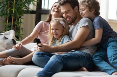 Küçük çocuklu mutlu ebeveynler evde cep telefonu kullanıyor.