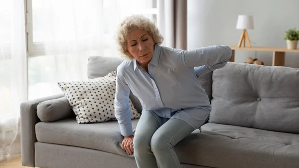Old woman gets up off the sofa feels repeated low backpain — Stock Photo, Image