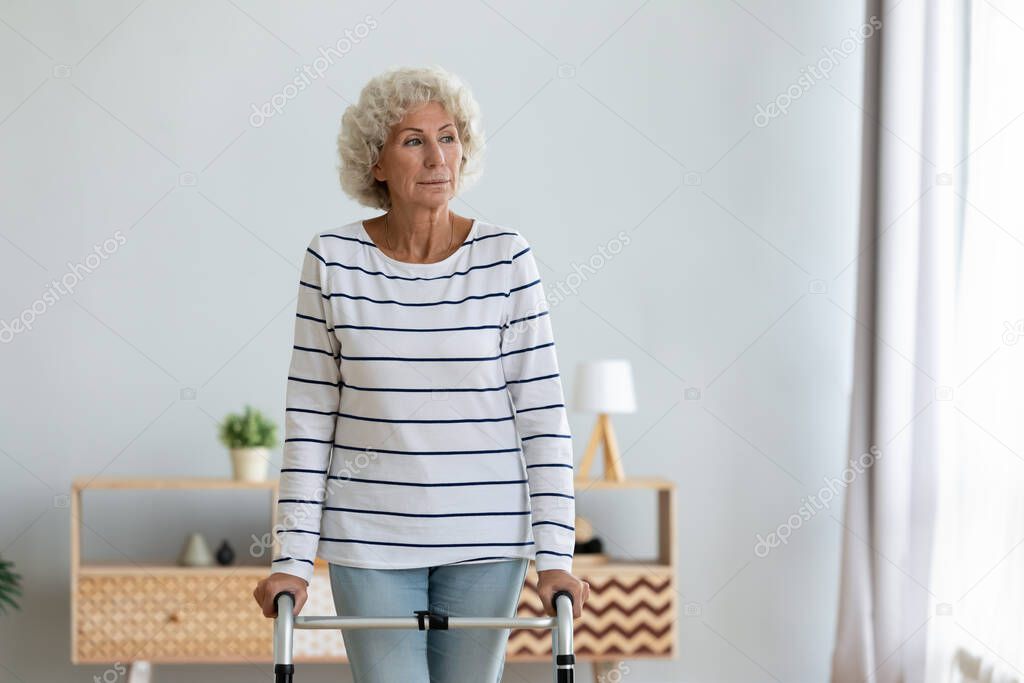 Elderly woman standing in living room holding walking frame